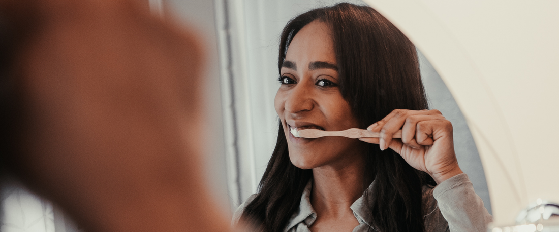 Young woman brushing her teeth in a bright bathroom with a Nudge toothpaste tube on the counter.